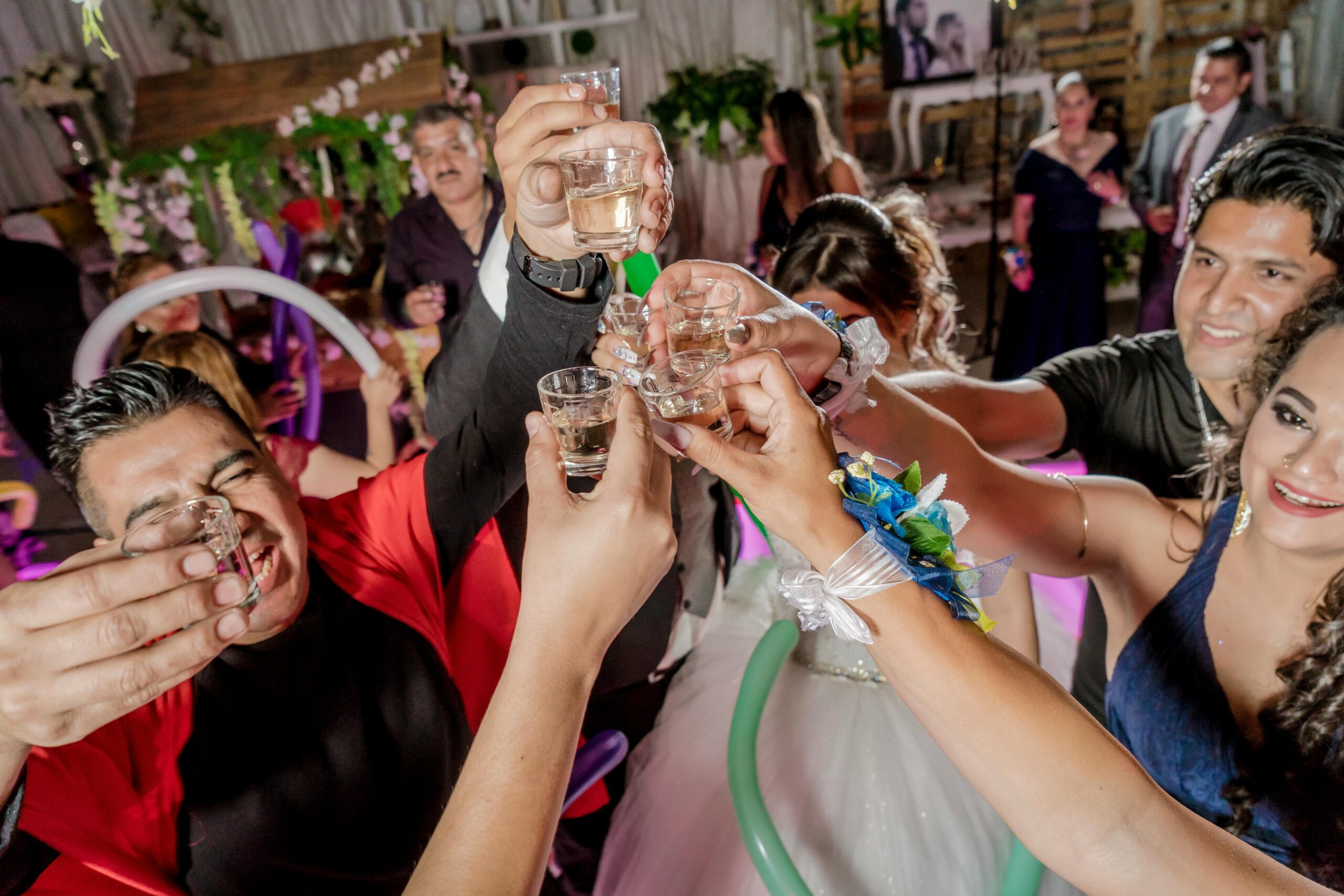 A diverse group of adults raising glasses in a cheerful toast at a lively indoor celebration.