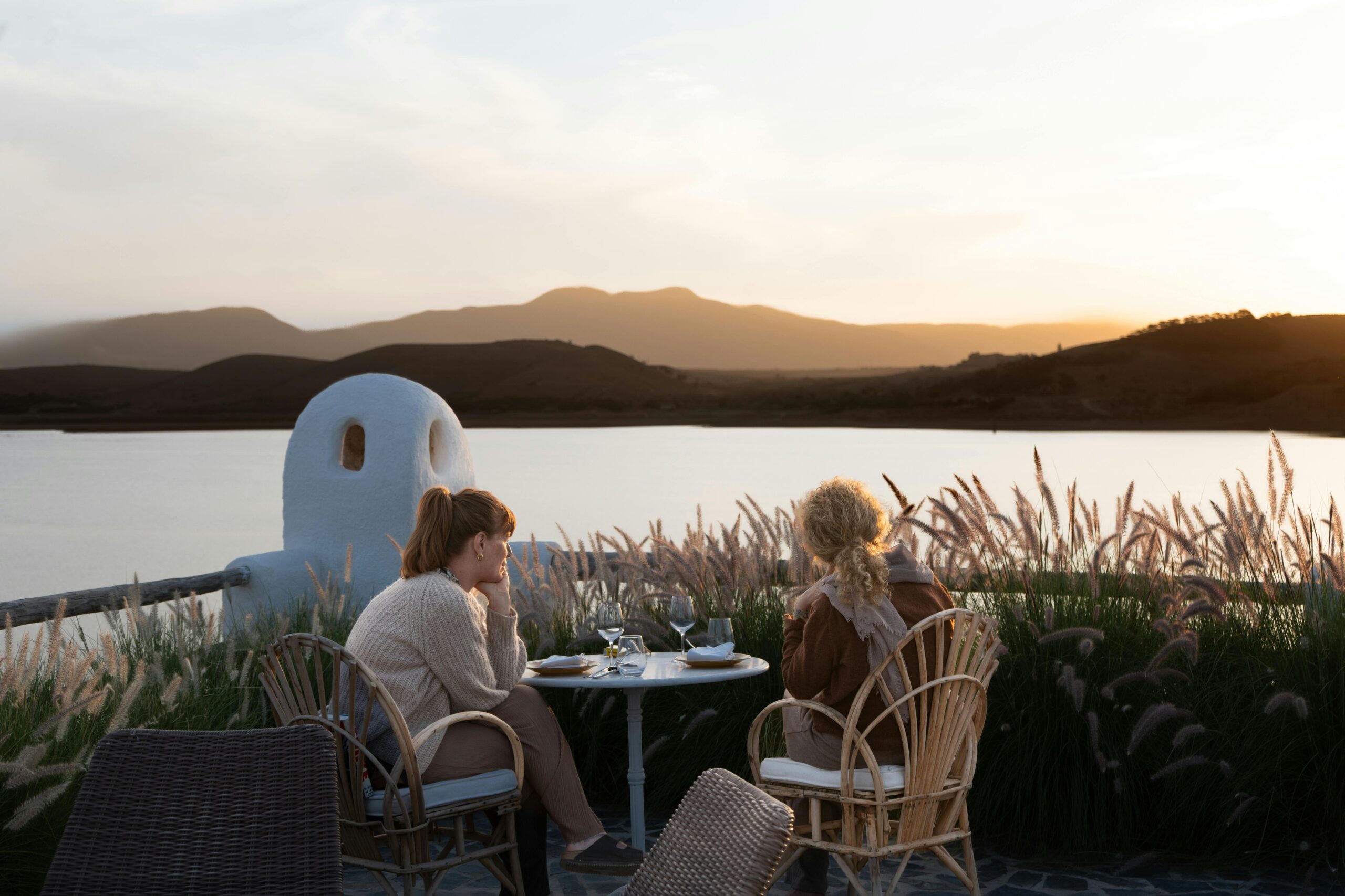 Two adults enjoying a lakeside meal at sunset, surrounded by serene nature.